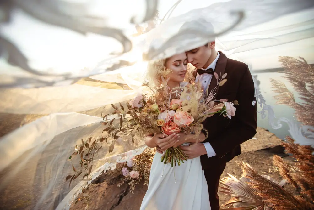 bride-groom-near-wedding-decoration-ceremony-cliff-rock-near-water-sunset-veil-flying-from-wind